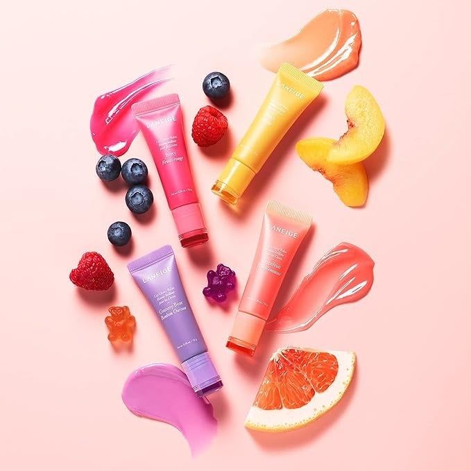 An assortment of skincare products with fruit slices and gummy bears placed on a soft pink backdrop.
