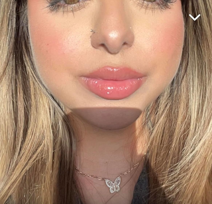 A close-up of a person wearing glossy lip makeup, paired with a delicate butterfly pendant necklace.