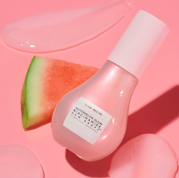 A pink bottle resting next to a fresh slice of watermelon.
