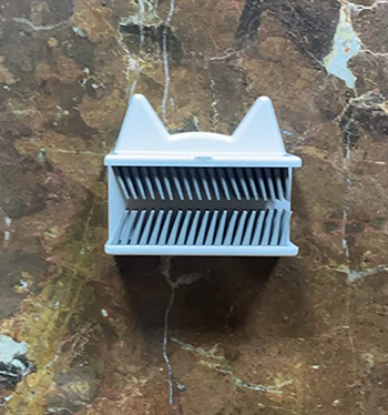 A small silicone bristle attachment shaped like a cat with white ears, attached to the wall.