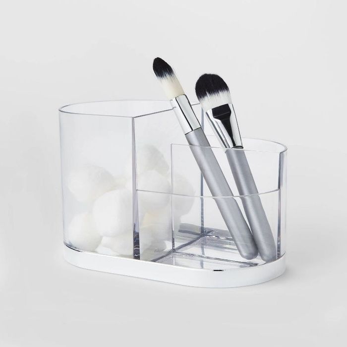 A silver and clear vanity tray holding brushes and cotton balls.