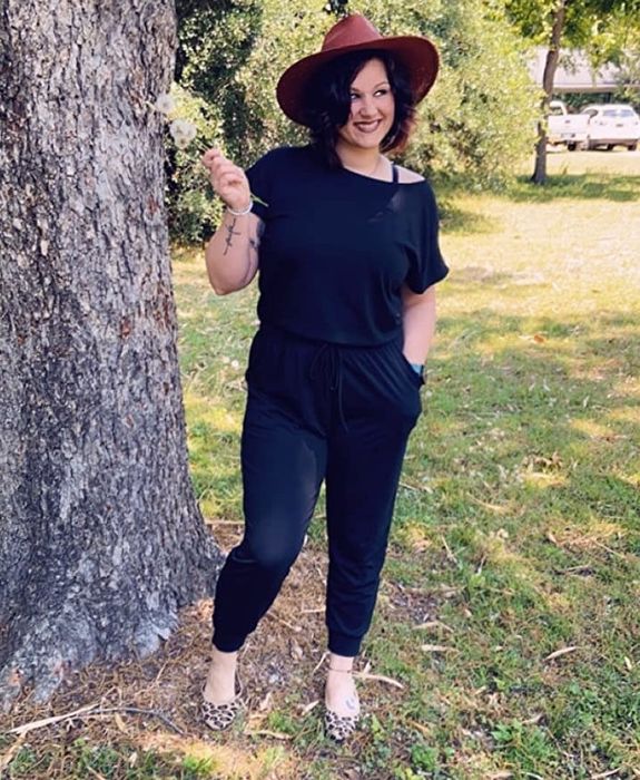 A reviewer wearing the jumpsuit in Black, styled with leopard print flats and a warm brown wide-brimmed fedora