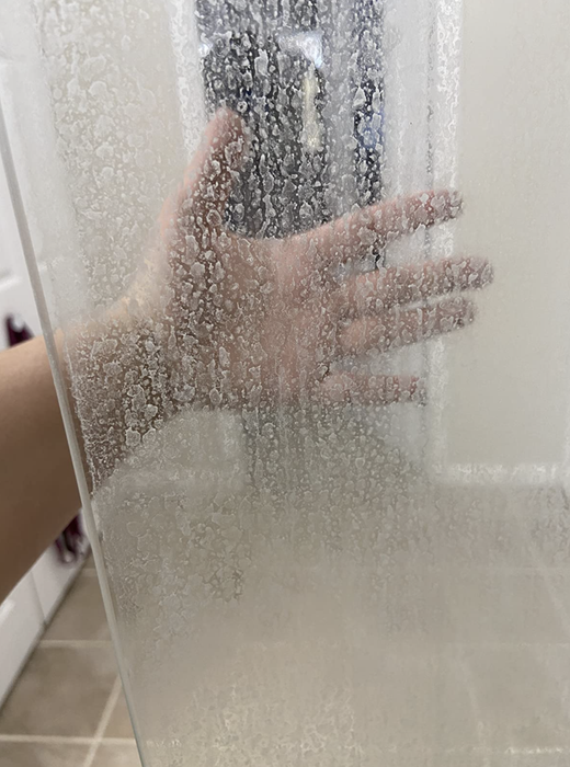 A glass shower door appears to be covered in fog from accumulated hard water stains.