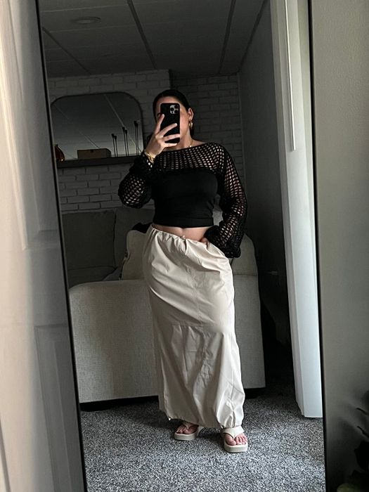 A reviewer takes a mirror selfie, wearing a black mesh top and a cargo skirt, paired with open-toe sandals.