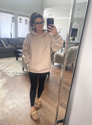 A reviewer wearing an oversized cream-colored hoodie