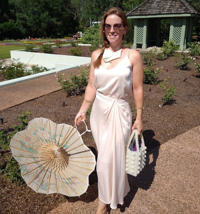 A reviewer wearing the off-white silky cami, paired with a silk skirt and holding a parasol while outside