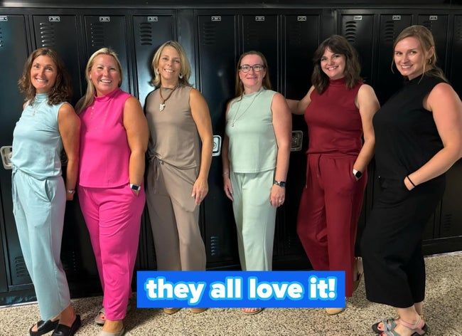 Six people stand in a hallway, each wearing a sleeveless jumpsuit in different styles, all posing and smiling.