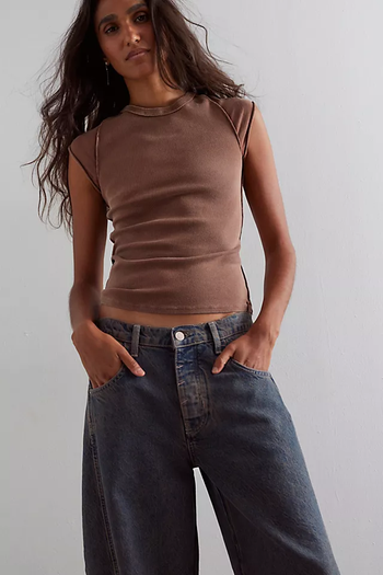 A person confidently poses in a sleeveless, casual top paired with wide-leg jeans.