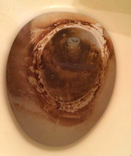 A build-up of brown grime inside a toilet bowl.