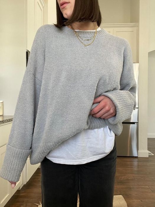A person wearing a cozy oversized sweater over a white shirt, styled casually, standing indoors. No visible text or celebrities
