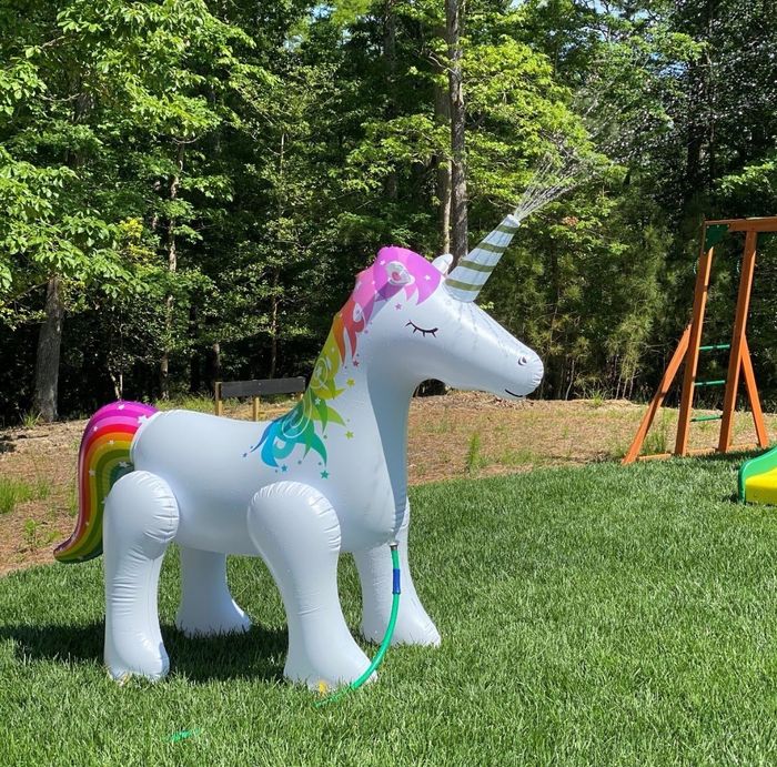 An inflatable white unicorn with a rainbow-colored tail and mane spraying water from its horn