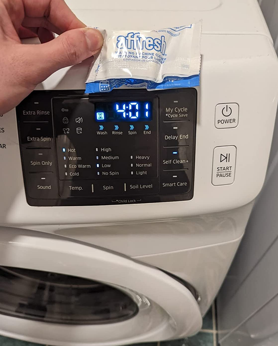 A reviewer holding a cleaning tablet in front of their washing machine