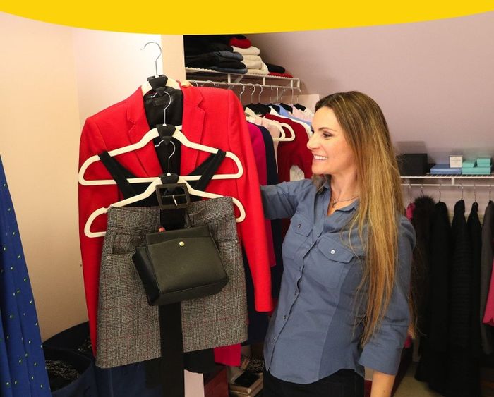A model in a blue shirt smiles while organizing a stylish outfit in a closet, showcasing a red blazer and a gray skirt. Text: 