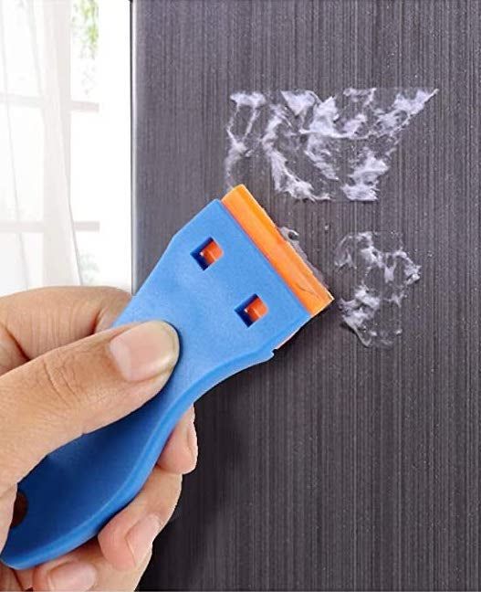 A hand using the scraper to remove sticky residue left by a sticker