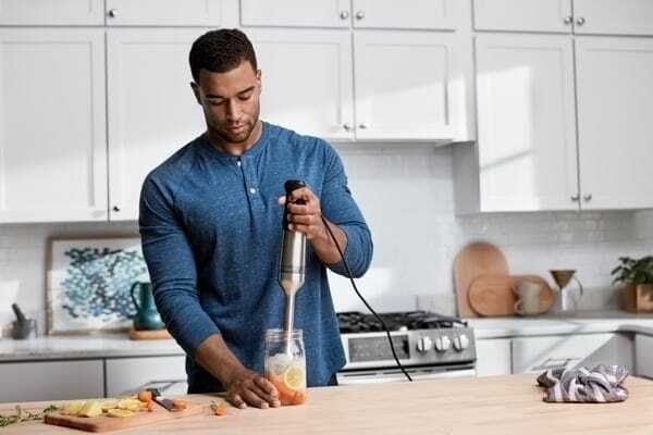 A person using the immersion blender to make an iced drink inside a glass jar