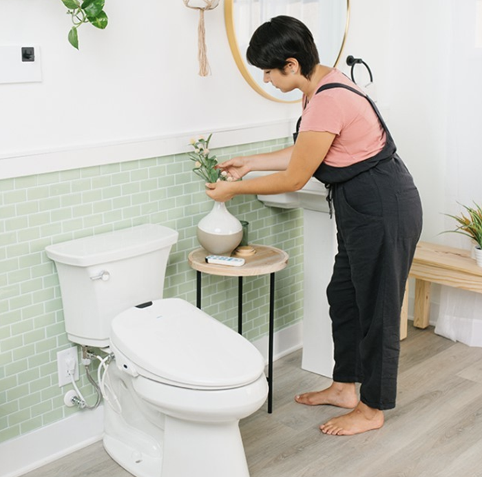 The toilet seat affixed to a tank in a chic bathroom, with a person standing beside it.