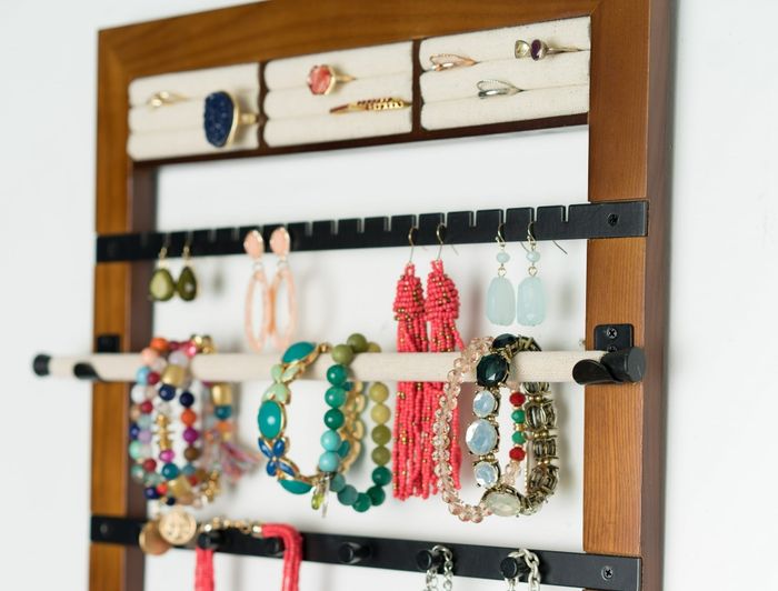 A wooden, wall-mounted jewelry organizer neatly displaying a variety of rings, earrings, bracelets, and necklaces in an accessible, organized way.