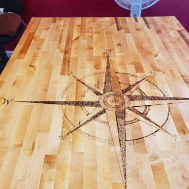 A reviewer's rose-shaped compass design burned into the surface of a wooden tabletop.