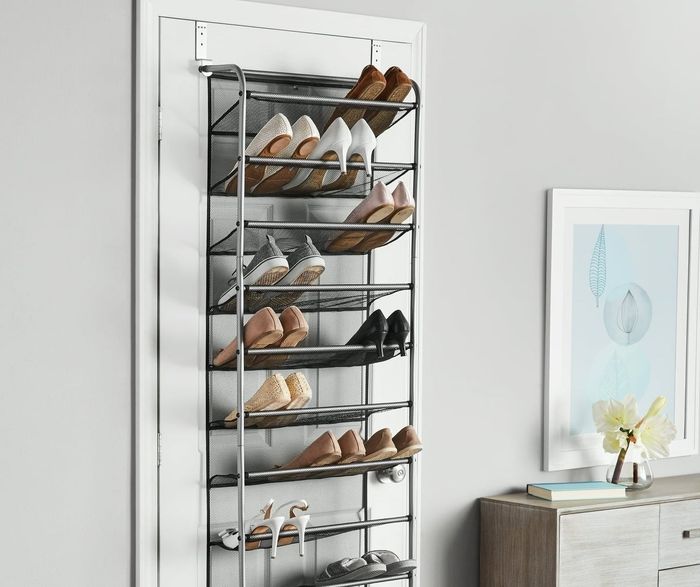 An over-the-door shoe organizer with shelves stacked with various shoes, positioned next to a cabinet and stylish decor on a hardwood floor