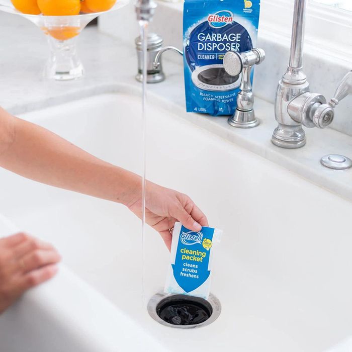 A hand placing the packet of garbage disposal cleaner into a drain