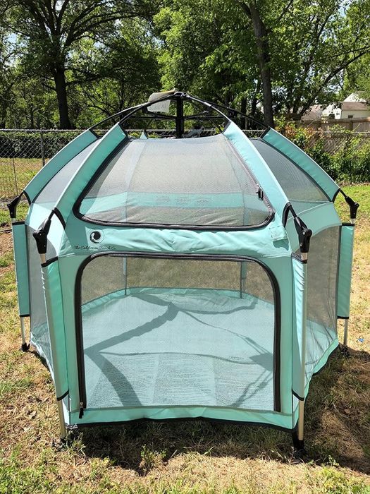 A lightweight, mint green mesh playpen set up outdoors on grass