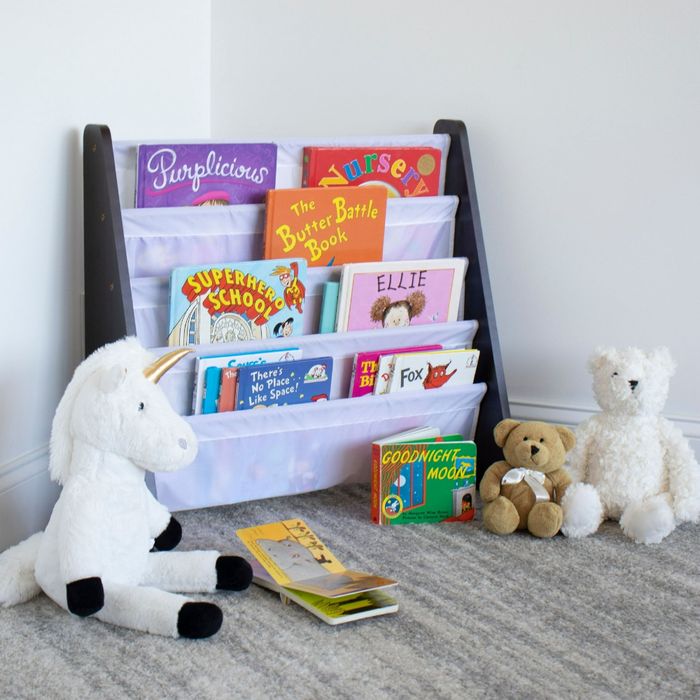 A collection of stuffed unicorns and bears gathered around a children's book rack filled with a variety of books, including 