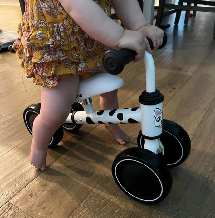 A toddler riding a small black-and-white balance bike indoors