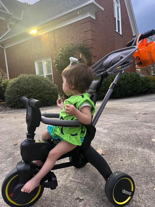 A toddler in a green outfit comfortably sitting in a tricycle stroller
