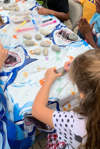 A birthday party scene with a table full of kids painting rocks