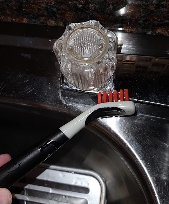 A reviewer using one of the brushes to clean a faucet knob, making it look brand new