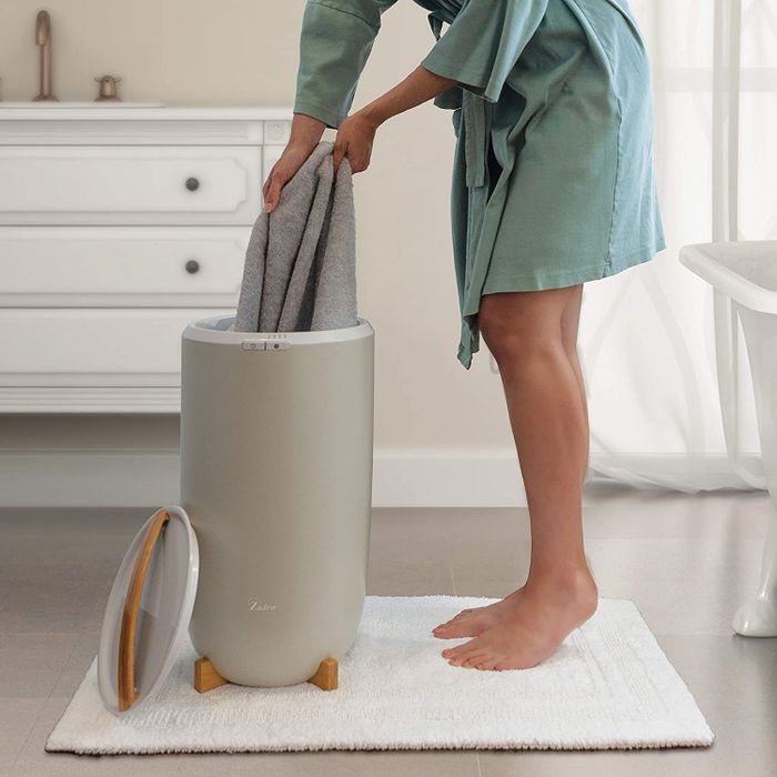 A person taking towels from an upright towel warmer, enjoying the comfort it provides.