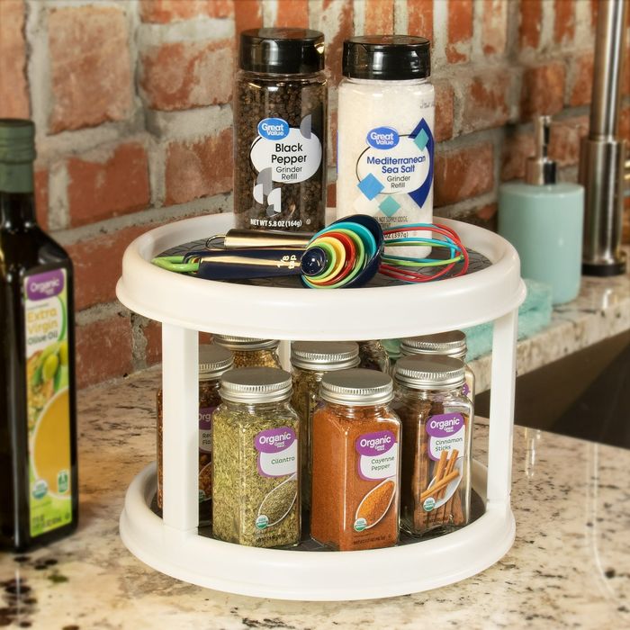A tidy kitchen countertop featuring a two-tier spice rack with a variety of spice jars, black pepper, Mediterranean sea salt containers, and colorful measuring spoons