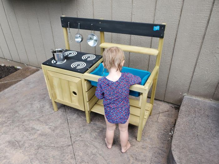 A photo of a toddler enjoying playtime at their mud kitchen outside