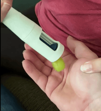 GIF of a reviewer using a grape cutter to slice grapes into quarters