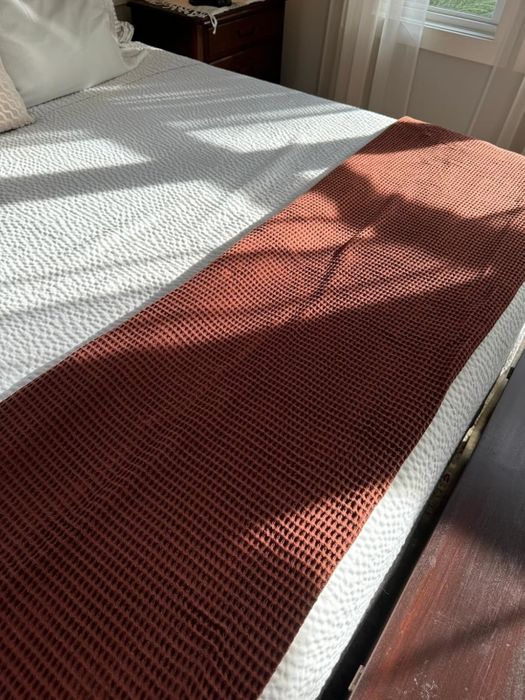 A neatly made bed with a textured throw blanket draped over the foot, creating a cozy and inviting look.