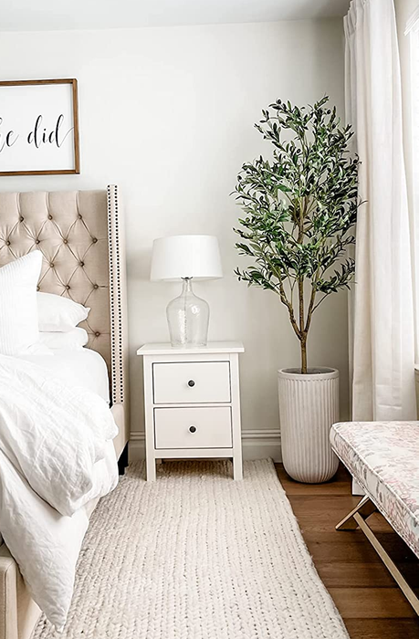 a photo showcasing a reviewer's olive tree placed in the corner of a bedroom