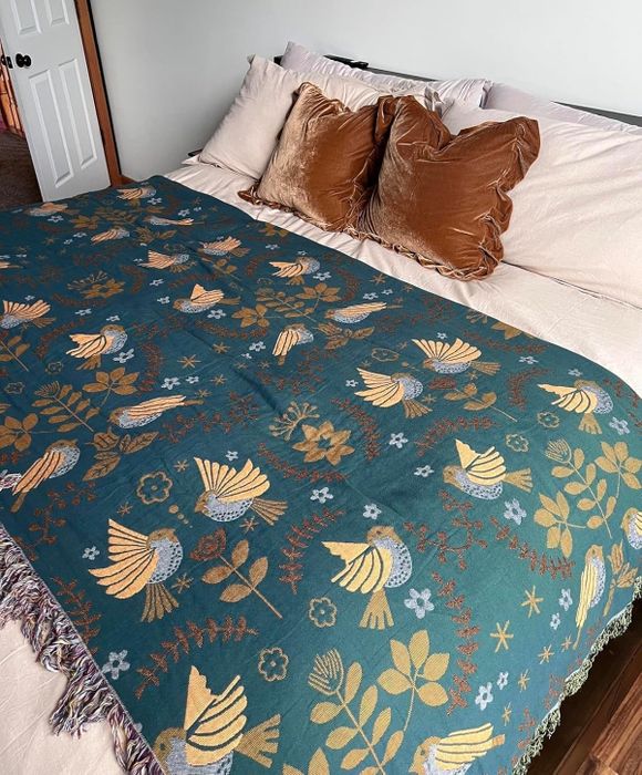 A plush bedspread adorned with a nature-inspired design featuring birds and flowers, elegantly placed over a tidy bed with decorative pillows.