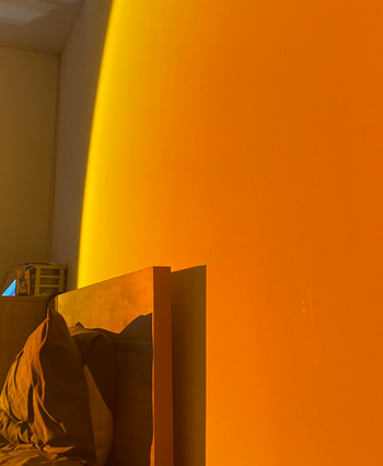 Sunlight casting a warm, inviting glow across a bedroom wall, gently illuminating a bed and its headboard.