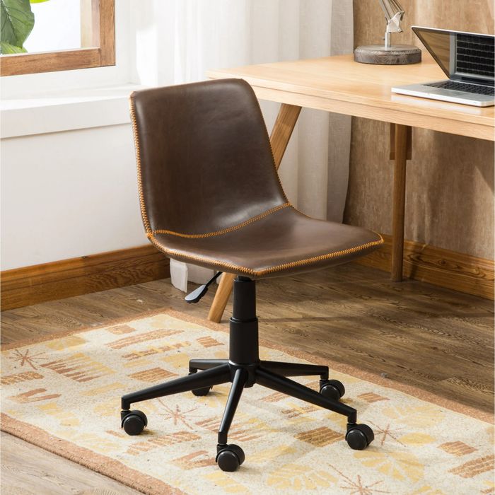 An antique brown leather office chair with adjustable height and wheels, positioned beside a wooden desk with a laptop and books in a cozy home office setting.