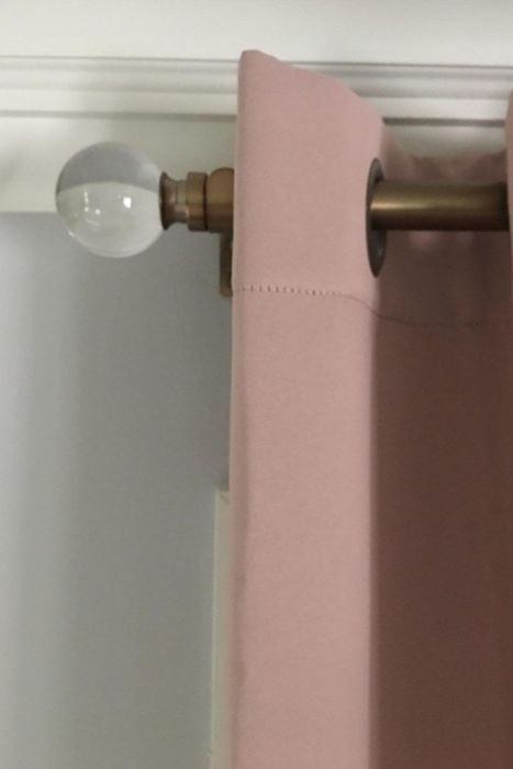 A brass curtain rod supporting pale pink curtains