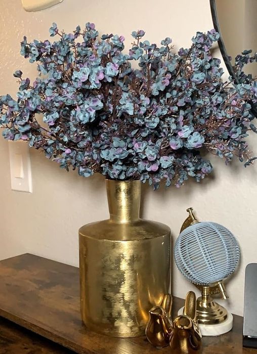 A charming display on a wooden table featuring a gold vase with artificial flowers, a small blue fan, and gold bunny figurines. A smartphone and charger are also visible in the arrangement.
