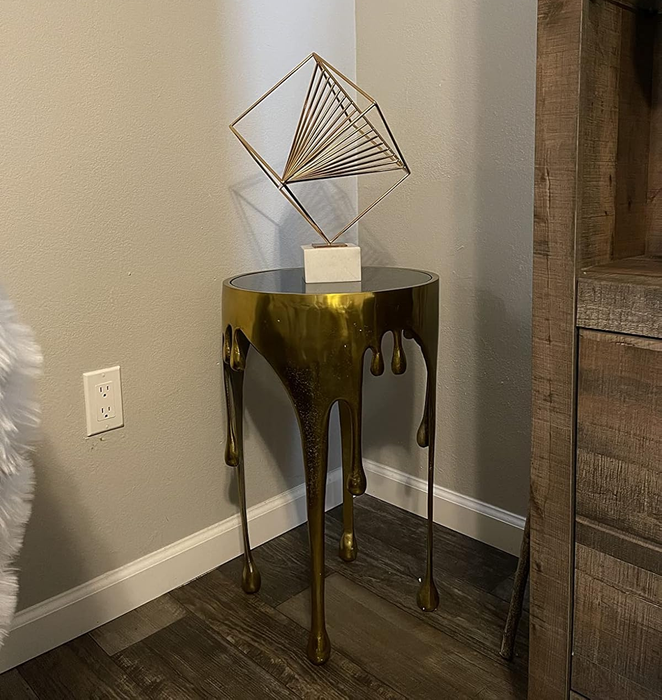 A one-of-a-kind side table featuring a melting effect, topped with a geometric artwork. This modern decor piece is set up next to a wall outlet in an indoor setting.