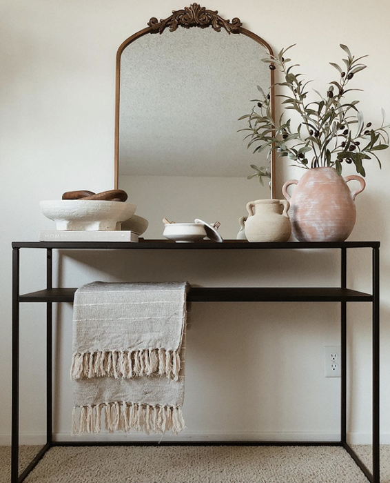 An arched mirror featuring gilded details at the top, placed on an entryway table.