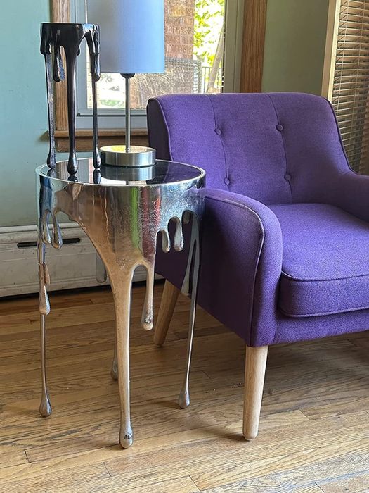 A reviewer’s photo of the sleek silver aluminum drip end table positioned beside a purple armchair.
