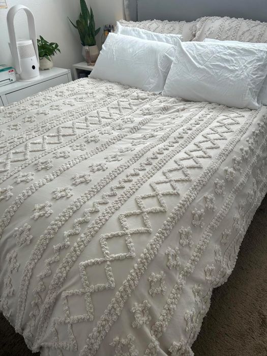 An intricately textured white bedspread on a neatly arranged bed, making it perfect for home decor