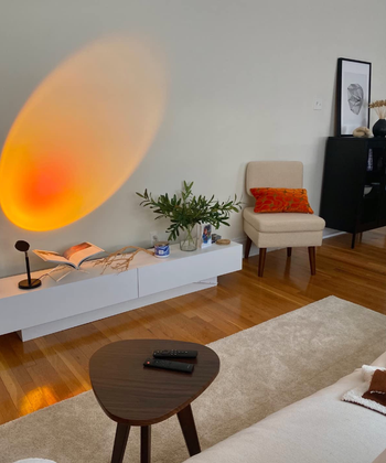 A contemporary living room featuring an oval wall light, a beige chair with an orange cushion, a plant, and a minimalist coffee table.