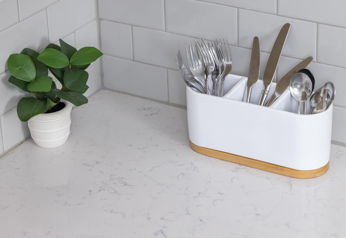 A tidy cutlery set in a white organizer sitting on a kitchen countertop, accompanied by a potted plant