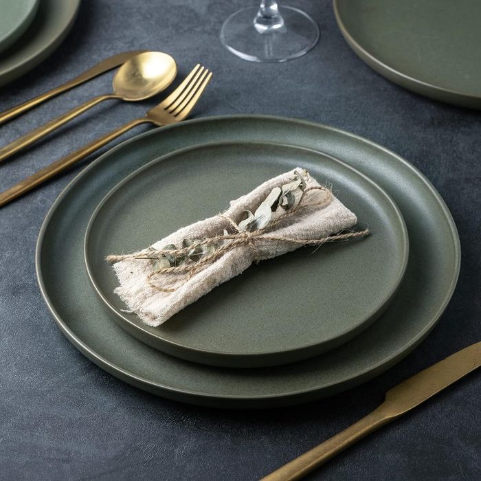 wavy green ceramic dinner plate with a salad plate resting on top, and the rest of the set neatly stacked behind it