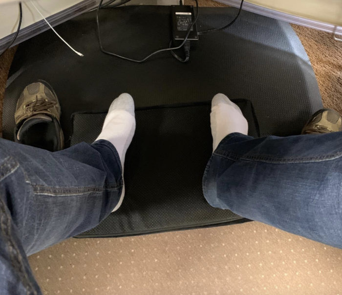 reviewer pictured using the black foot rest placed under the desk