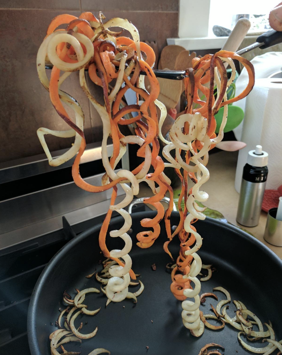 orange and white spiralized veggie noodles being held over a pan